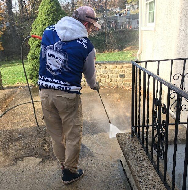 Men Wearing Industrial Wet Coat Cleaning Residential Driveway using Power Pressure Washer.